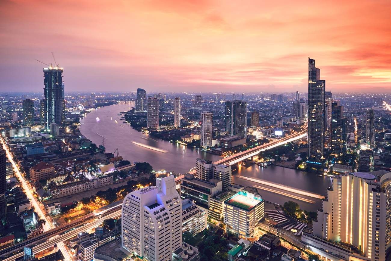 Bangkok at golden sunset, showcasing a busy city skyline with traffic-filled roads and the flowing Chao Phraya River.